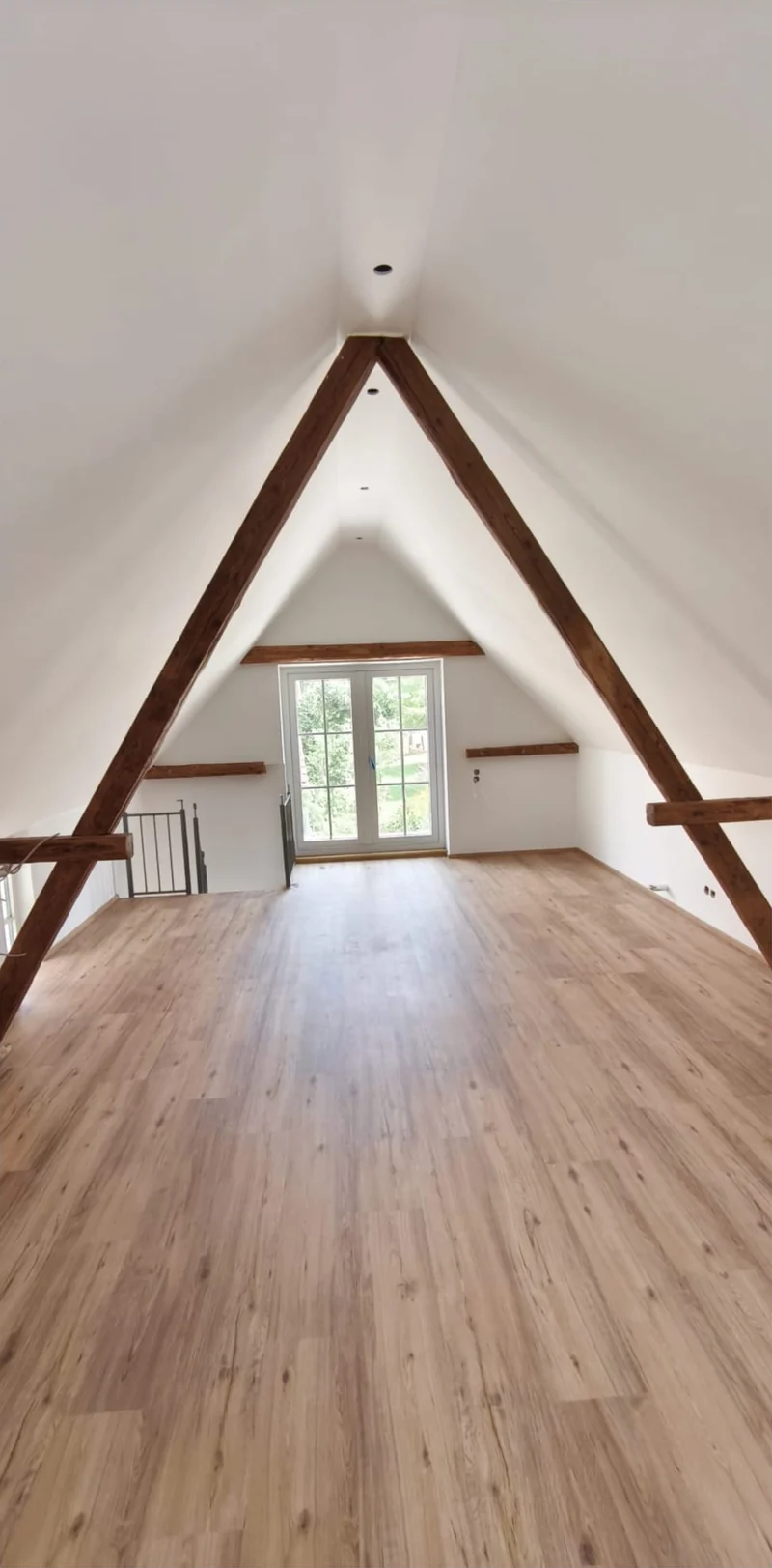 Ausgebautes Dachgeschoss mit weißen Schrägen, Holzbalken und Bodenbelag
